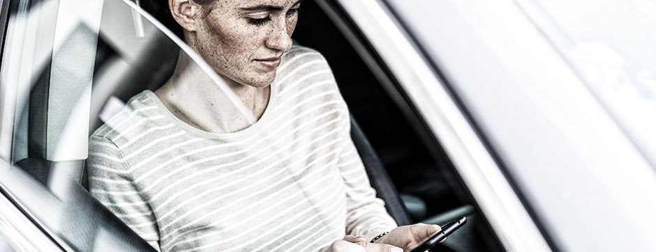 Junge Frau mit Smartphone auf dem Beifahrersitz