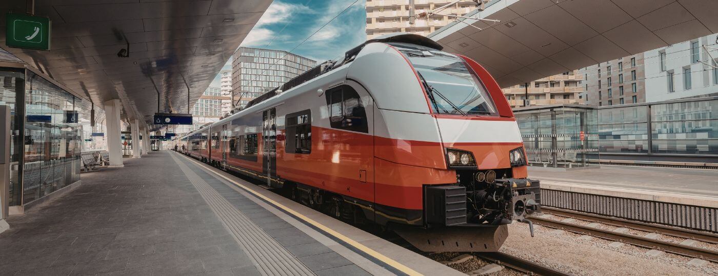 Moderner Regionalzug am Bahnsteig eines städtischen Bahnhofs Roter-weißer Regionalzug steht an einem modernen überdachten Bahnsteig mit Glasfassade und Stadtgebäuden im Hintergrund.