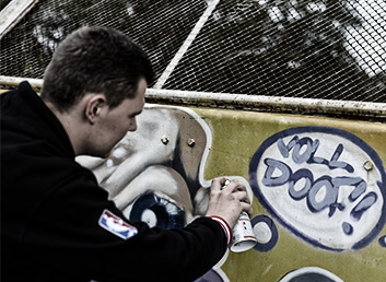 Ein Jugendlicher beschädigt eine Wand mit einem Graffiti.