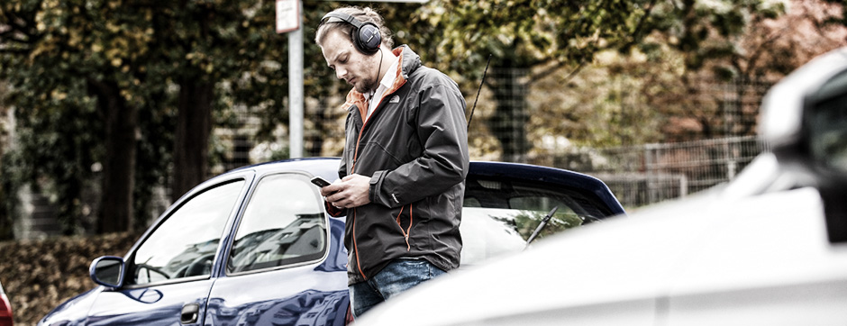 Mann läuft über Straße und schaut dabei auf sein Smartphone. Er trägt Kopfhörer.