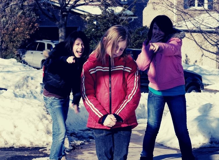 Zwei Mädchen lachen ein anderes Mädchen aus und zeigen mit dem Finger auf es.